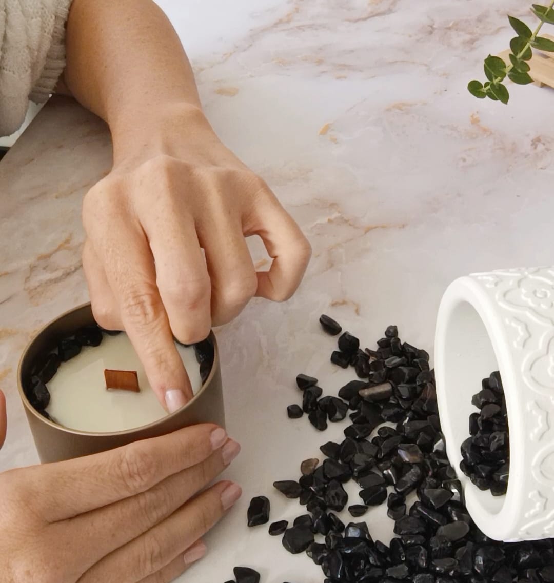 Mano colocando piedras de obsidiana en una vela artesanal como gesto de calma y presencia